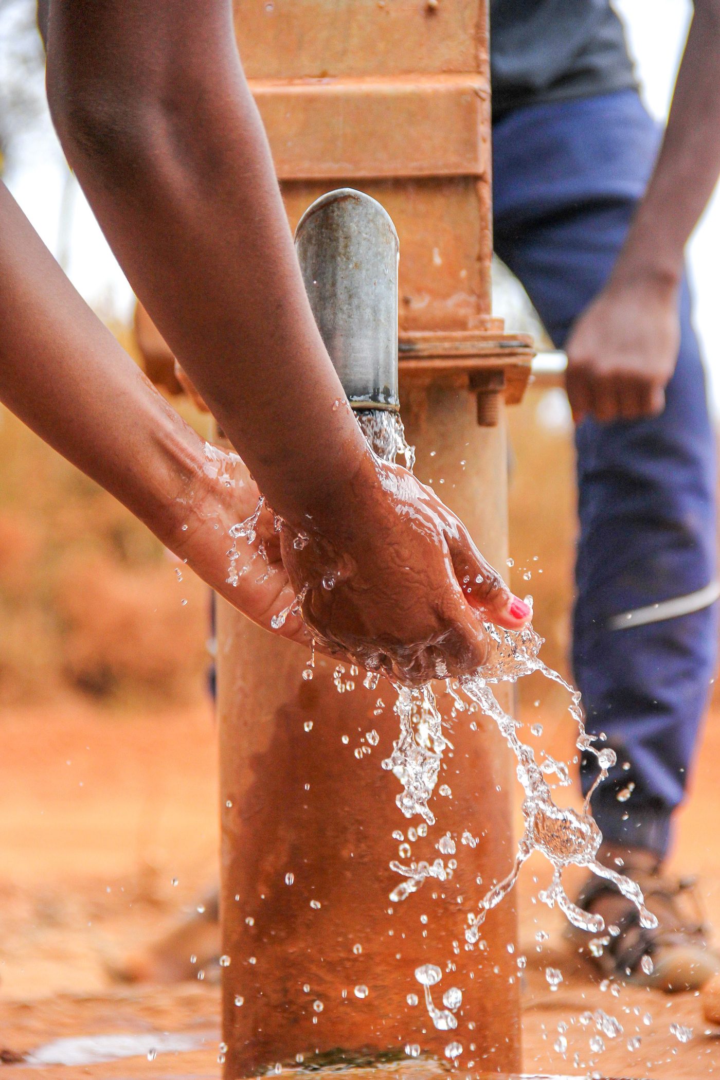 Hands washing under clean water from a hand pump